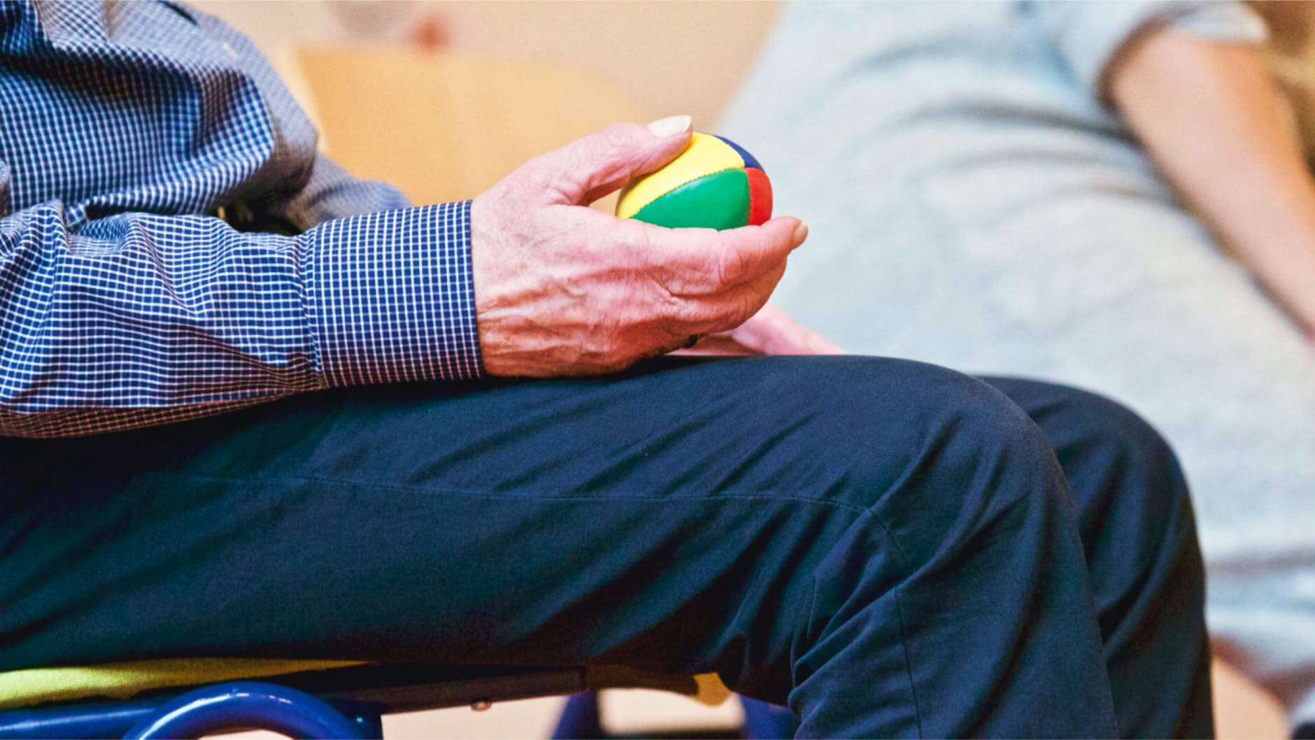 Persona mayor sentada con una pelota en la mano terapia ocupacional